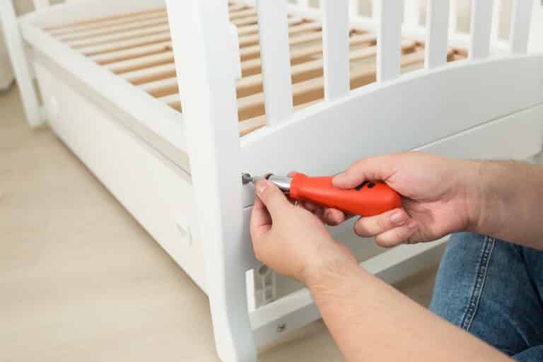 Closeup of handyman tightening the screws on white wooden bed